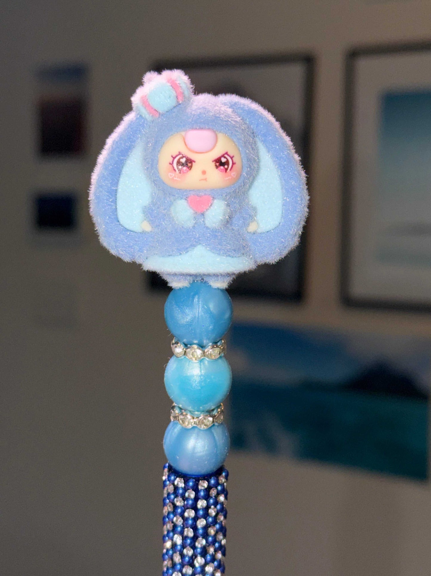 Blue decorative topper with a cartoon character inspired by a baby 3 with bunny ears and a crown and purple hair and angry eyes on a blue half bling pen on a blurred background