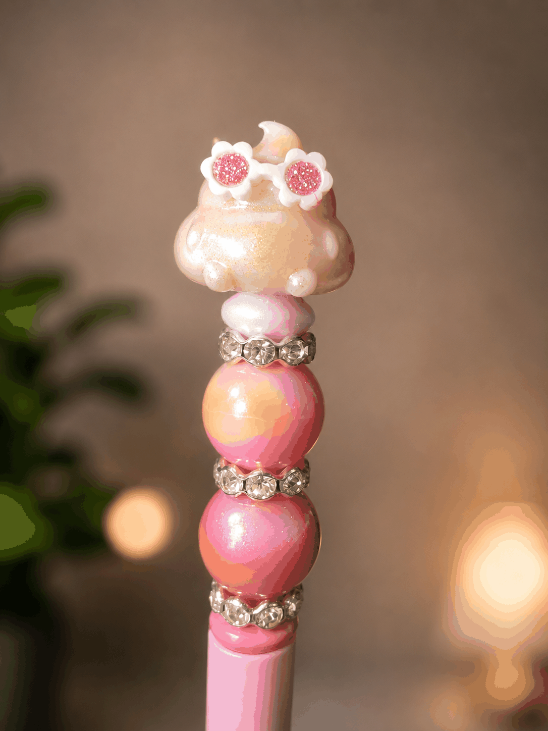 Handmade pink beaded pen featuring a cute poop cloud character wearing glittery flower sunglasses, accented with pastel peach, pink, and lavender ombré beads and sparkling rhinestone spacers.