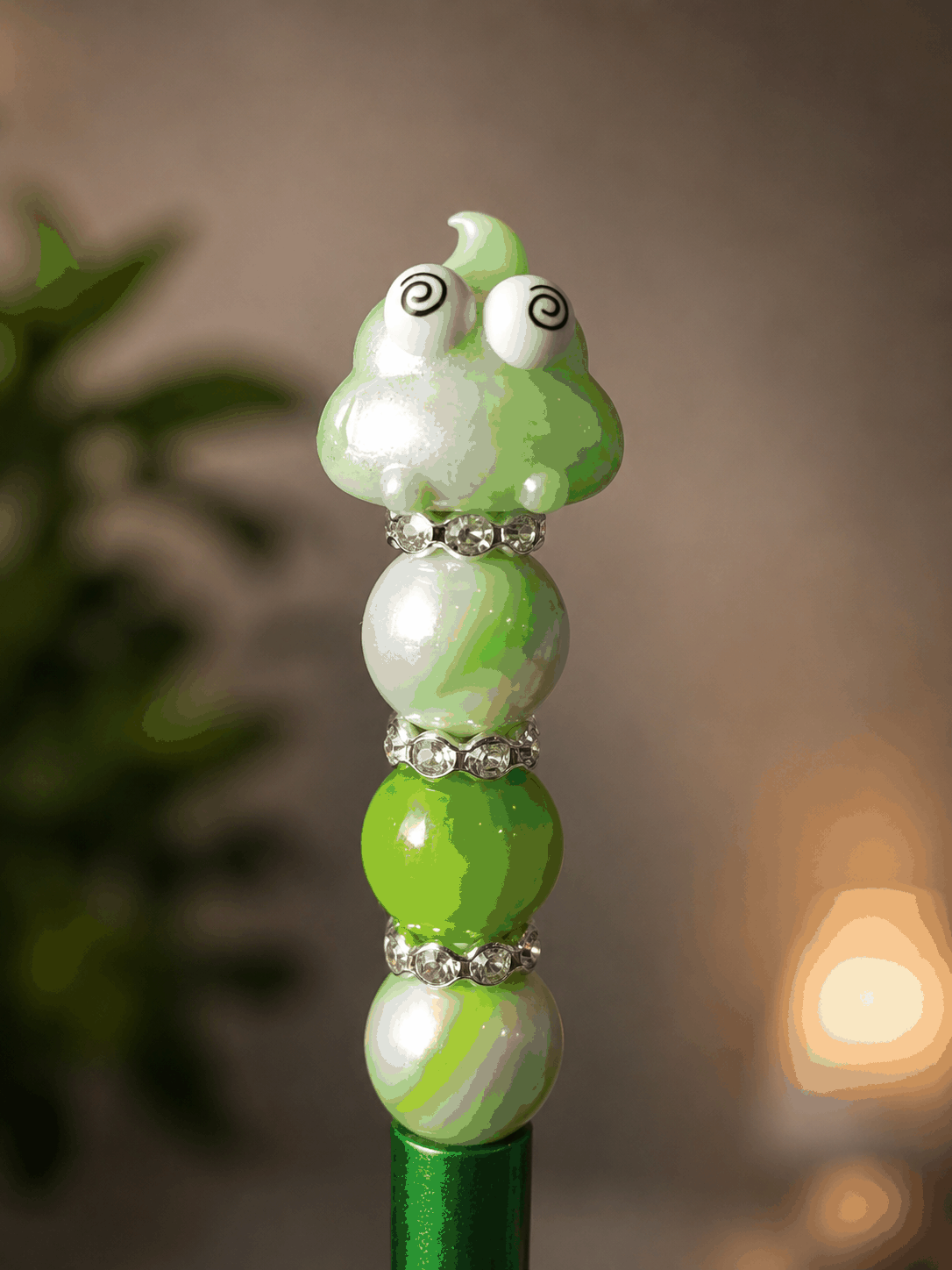Handmade green beaded pen featuring a cute kawaii poop character with spiral eyes, accented with pearlized green and white beads and sparkling rhinestone spacers, displayed as a fun novelty desk accessory.
