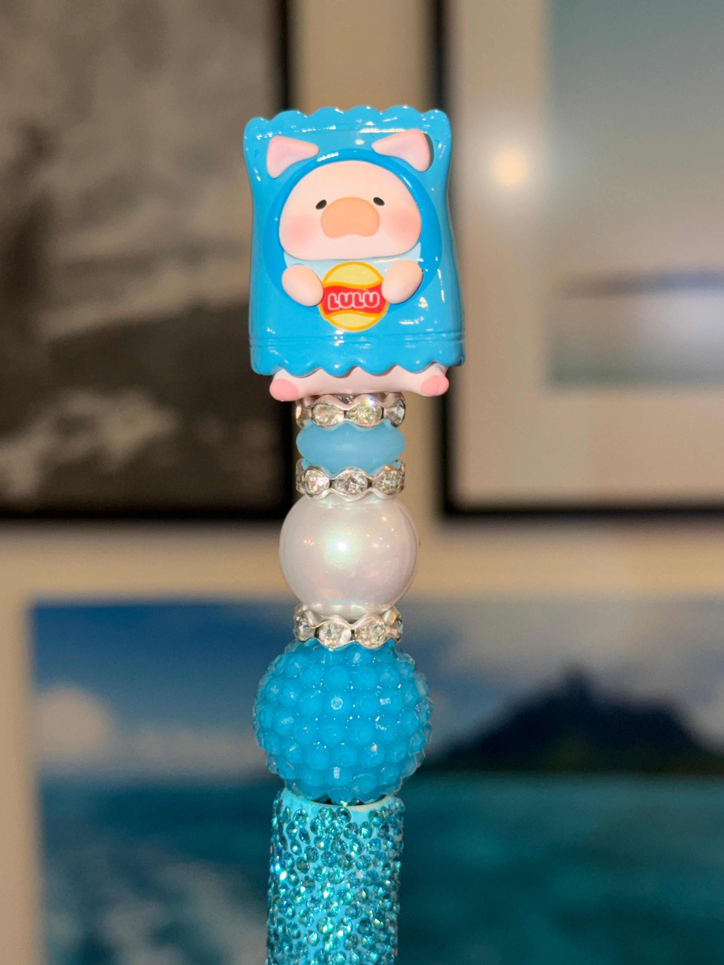 Lulu pig 3-D bean in a blue chips outfit with a yellow and red logo that says Lulu in the middle on top of blue white and rhinestone beads on a black pen