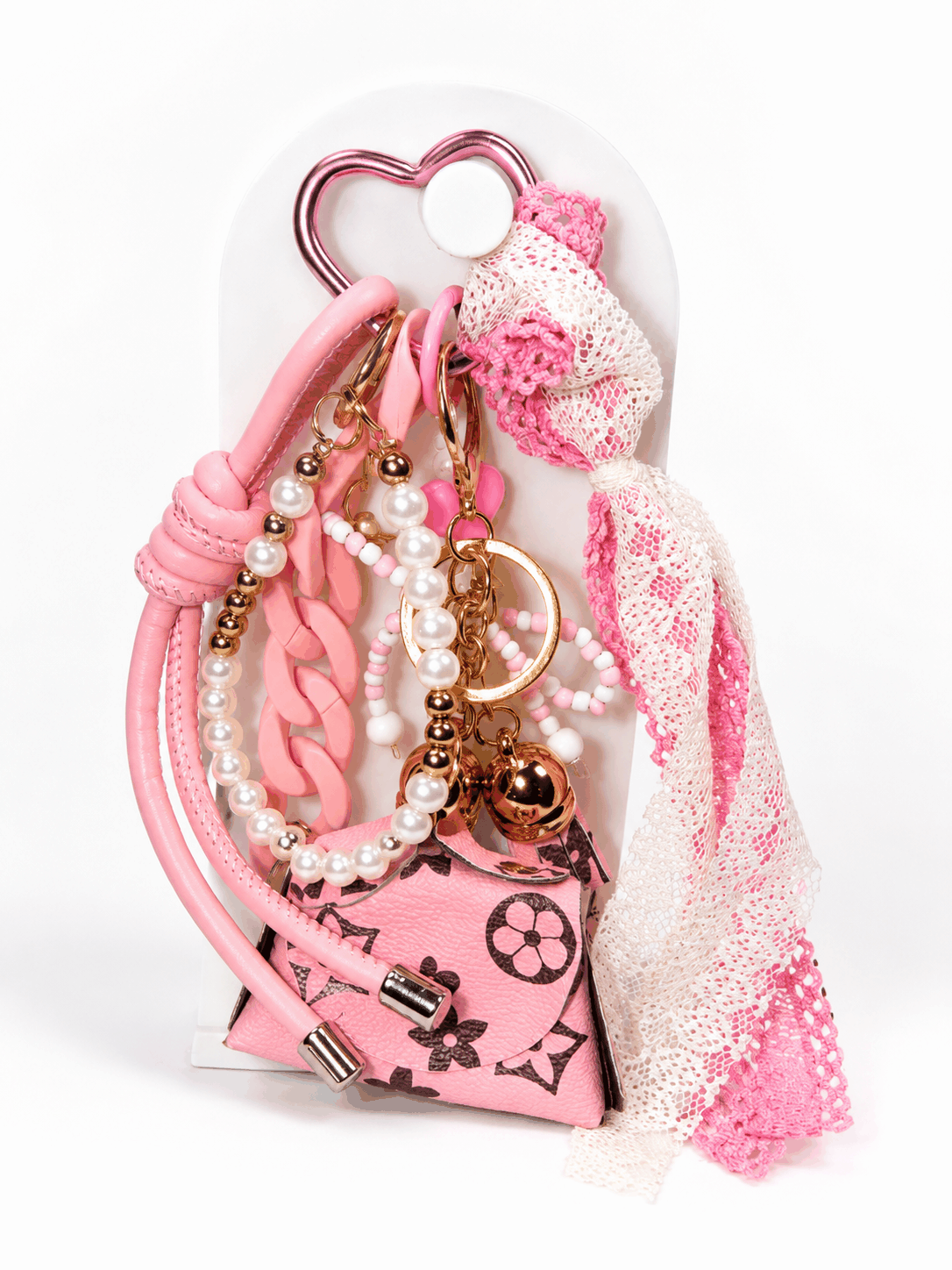 Pink coquette-style bag charm featuring a heart-shaped carabiner, pearl accents, pink lace bow, chunky pink chain links, and a designer-inspired mini purse charm displayed on a white stand against a clean white background.