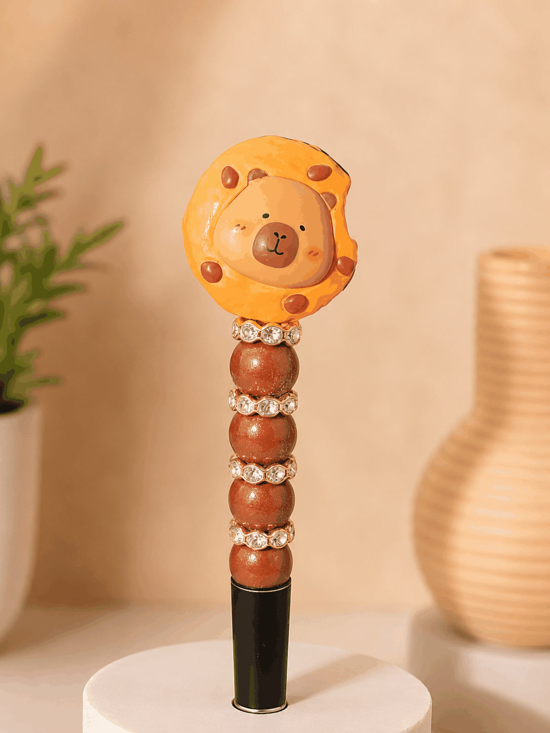 Handmade beaded pen featuring a cute capybara character nestled inside a cookie-shaped topper. The pen includes warm caramel-colored beads, sparkling rhinestone spacers, and a black pen barrel, creating a cozy bakery-inspired design perfect for journaling, planning, and desk decor.