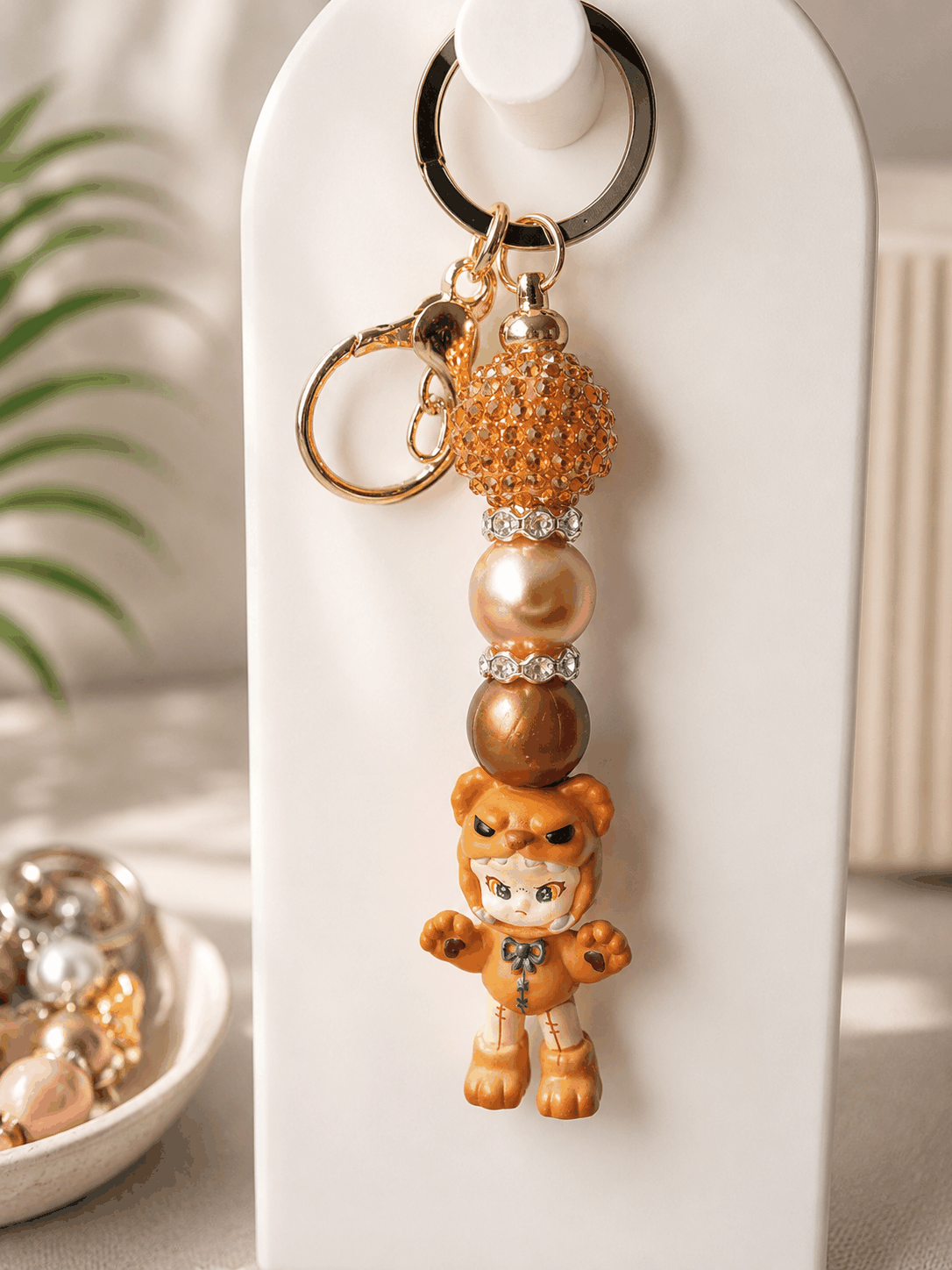 Authentic Dora Bean beaded keychain featuring a collectible Dora Bean charm with champagne and bronze pearl beads, crystal pavé accent bead, rhinestone spacers, and gold-tone hardware displayed on a neutral background.