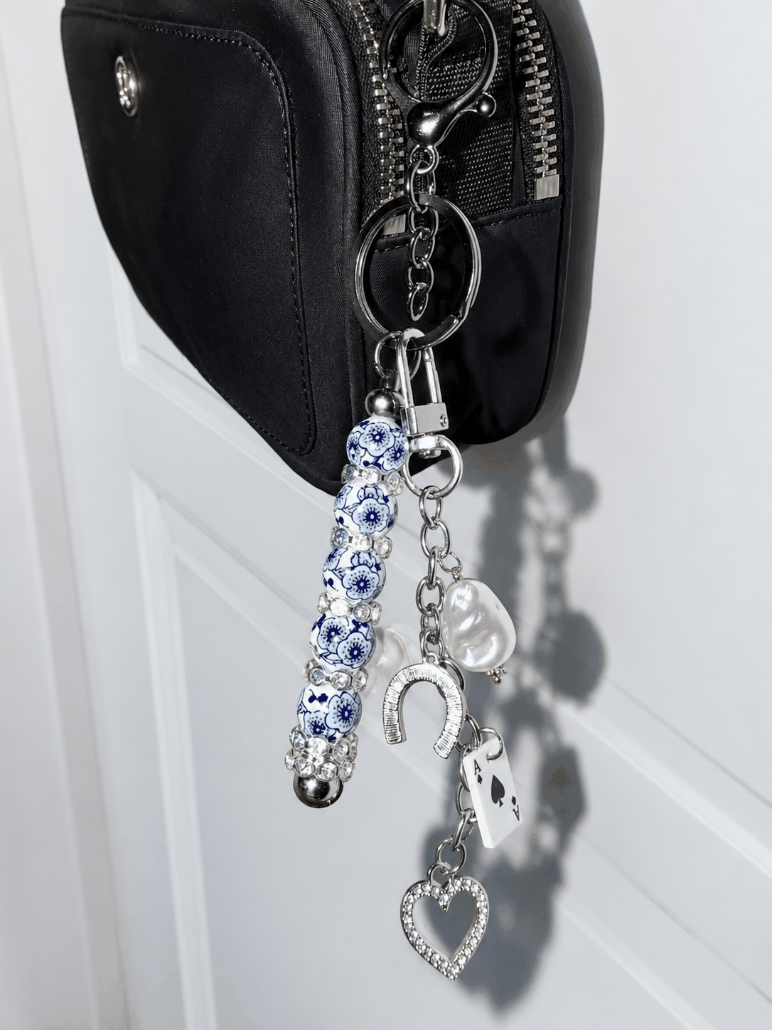 Handcrafted blue and white porcelain inspired beaded bag charm keychain with crystal horseshoe, Ace of Spades charm, pearl accent, and silver hardware displayed on a white background.