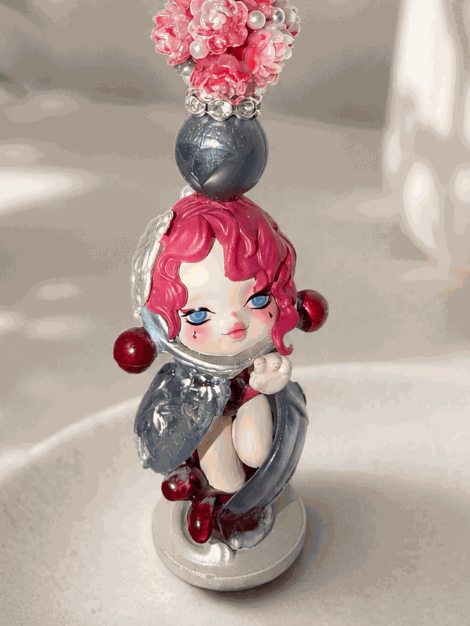 Handmade beaded keychain featuring an authentic pink-haired collectible doll charm with pink floral resin beads, gray pearl accents, sparkling rhinestone spacers, and silver hardware displayed on a neutral background.