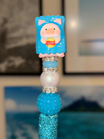 Lulu pig 3-D bean in a blue chips outfit with a yellow and red logo that says Lulu in the middle on top of blue white and rhinestone beads on a black pen