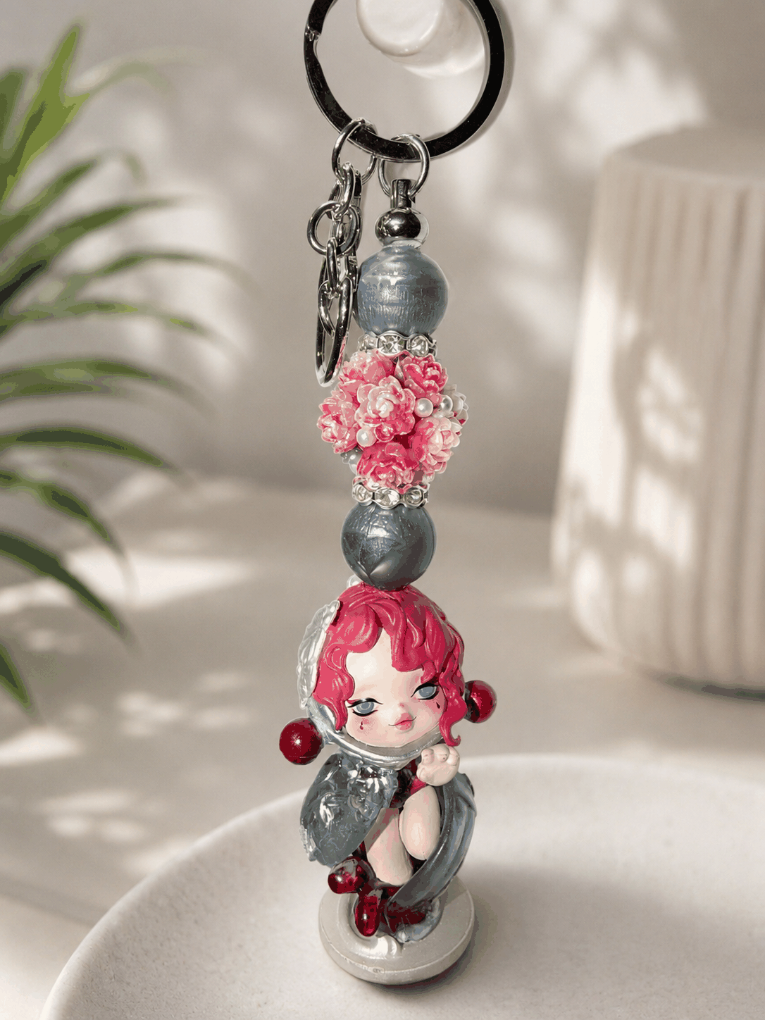 Keychain with a small figurine of a girl with pink hair and flowers on a light background