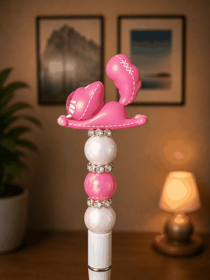 Handmade beaded pen featuring an authentic Pink Cat Bean collectible topper with stitched details and a glitter heart spade emblem, accented with pearl and pink beads, rhinestone spacers, and a white pen base.