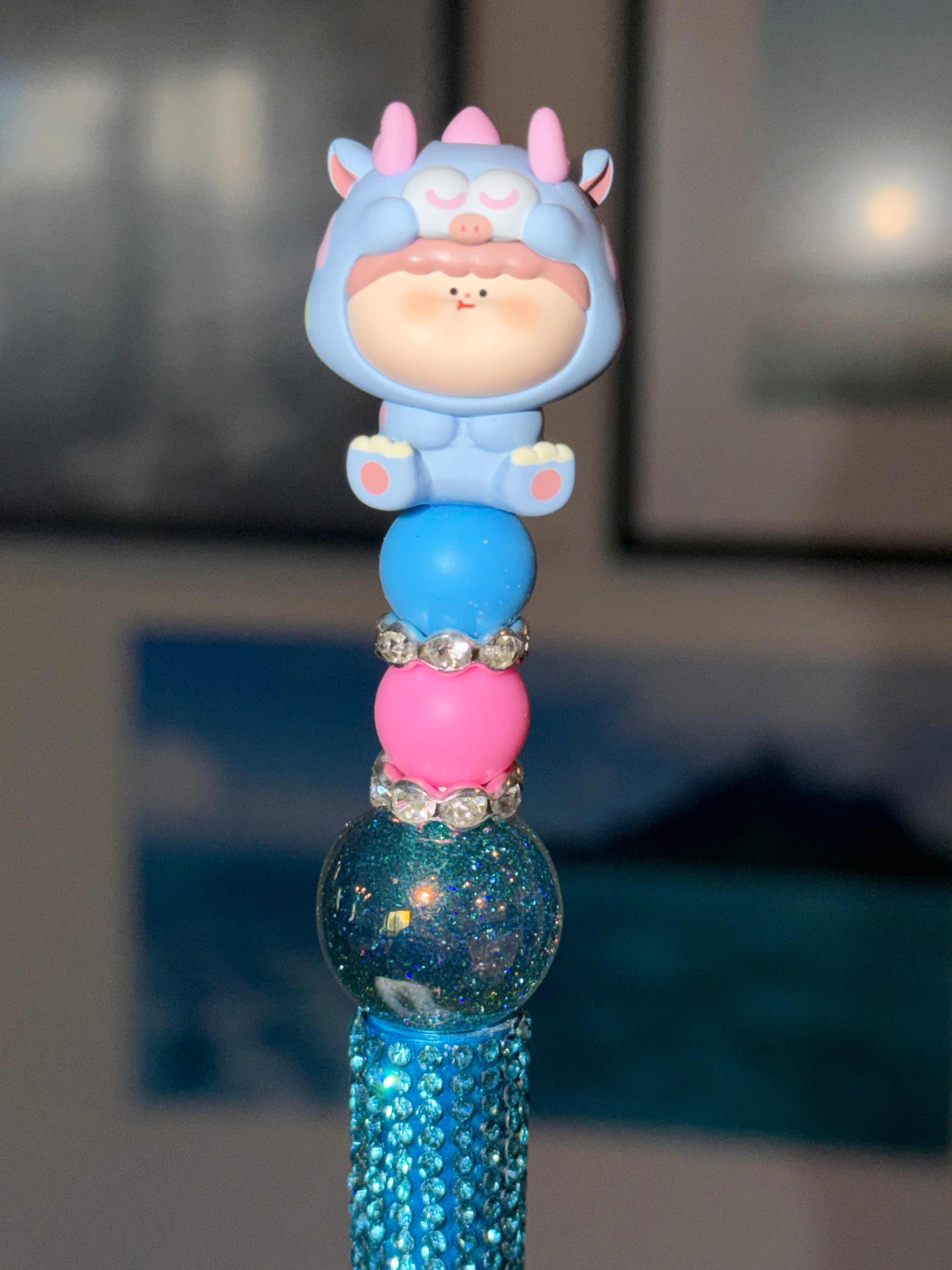 Dino Costume Baby Beaded Pen with blue pink beads and rhinestones, featuring a sleepy baby in blue horned monster onesie topper