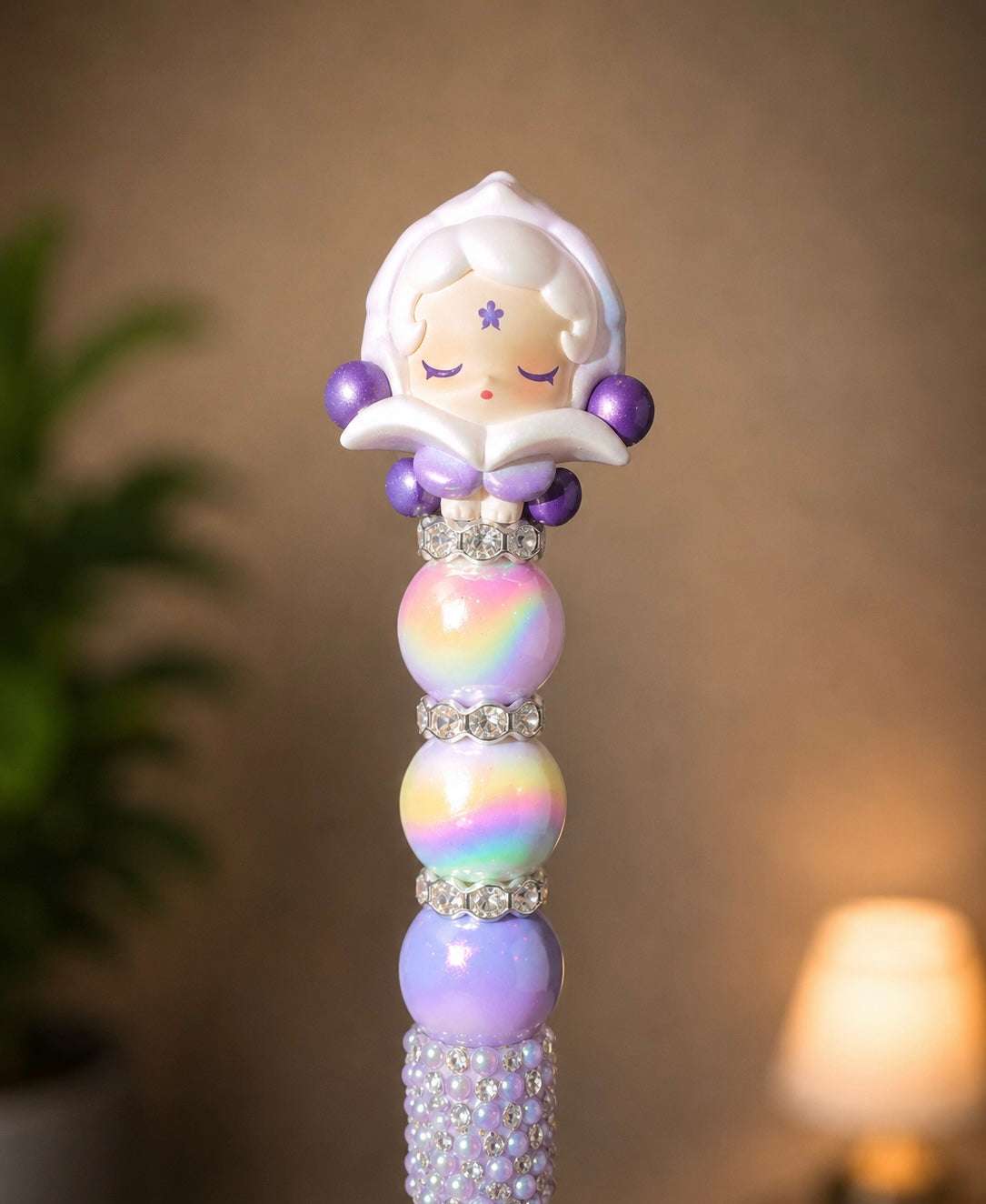 Handmade beaded pen featuring an authentic Skullpanda Pop Bean collectible topper with lavender accents, iridescent rainbow beads, sparkling rhinestone spacers, and a pearl-and-crystal embellished pen barrel.