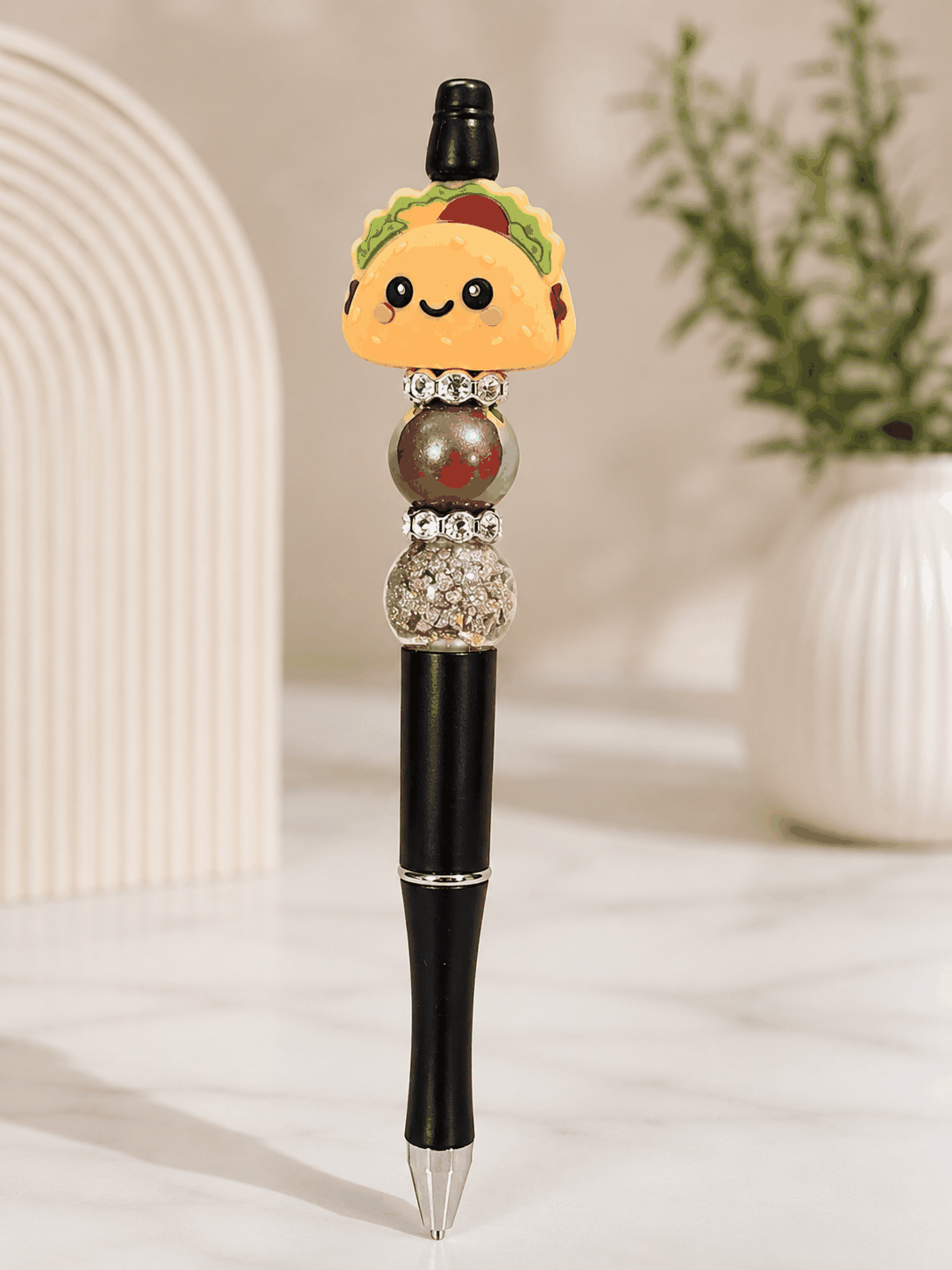 Black beaded pen decorated with a smiling taco topper, iridescent bead, glitter-filled bead, and rhinestone spacers for a fun food-themed writing accessory.