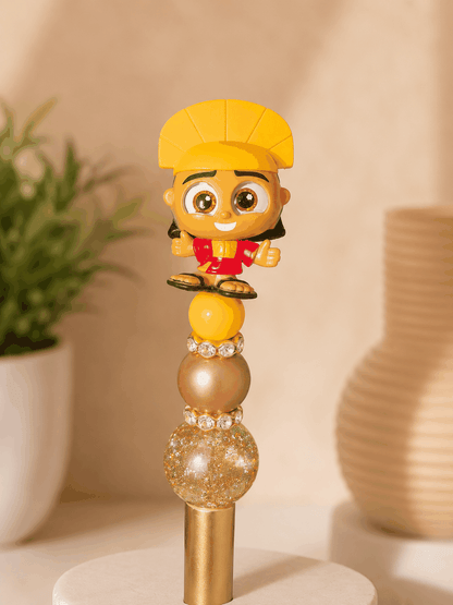 Handmade beaded pen featuring an authentic Kuzco Doorable character topper with gold glitter, champagne, and yellow accent beads separated by sparkling rhinestone spacers on a gold pen barrel. Perfect for Disney collectors and stationery enthusiasts.