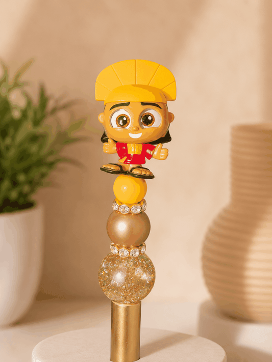 Handmade beaded pen featuring an authentic Kuzco Doorable character topper with gold glitter, champagne, and yellow accent beads separated by sparkling rhinestone spacers on a gold pen barrel. Perfect for Disney collectors and stationery enthusiasts.