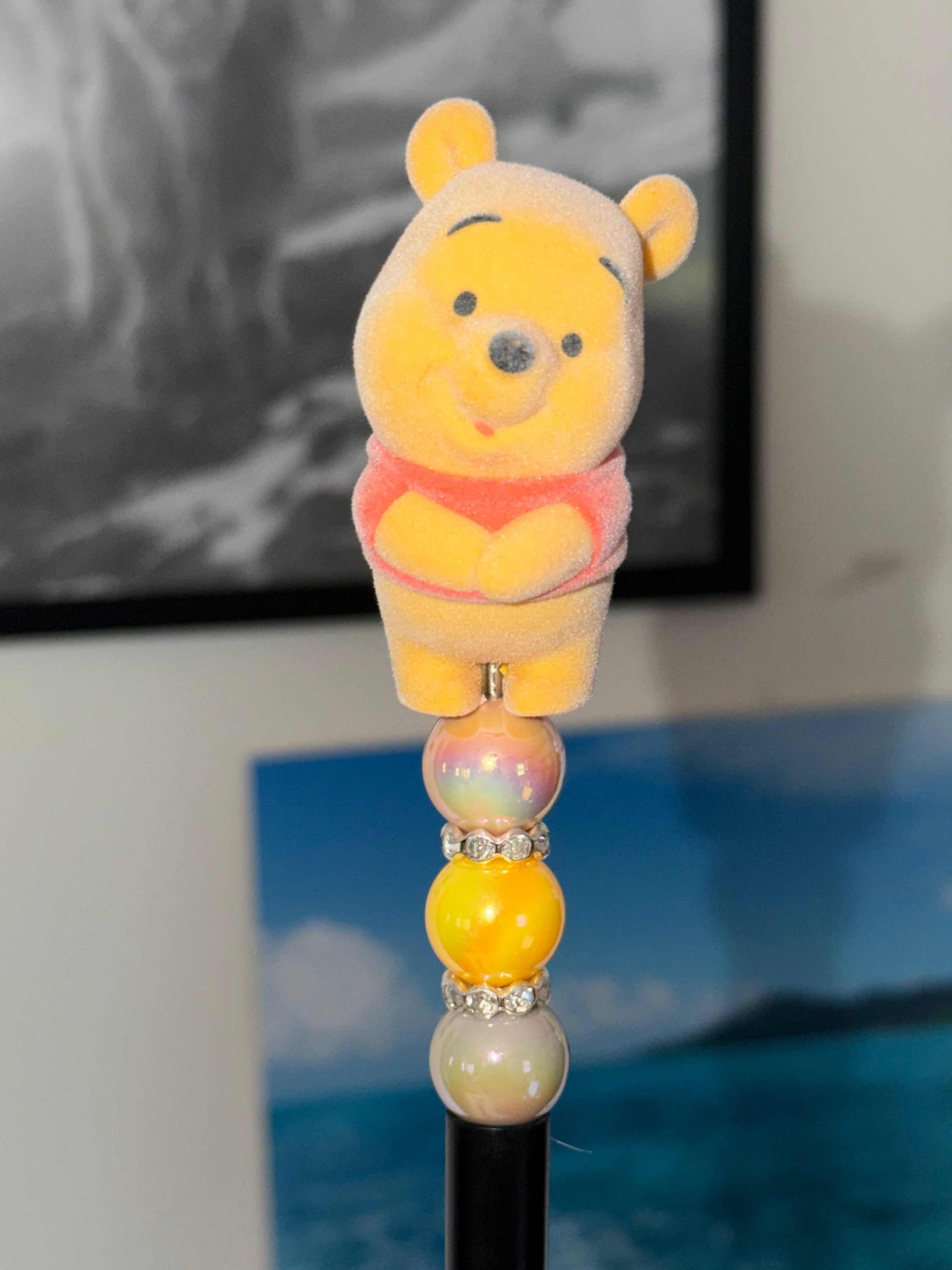 Handmade beaded pen featuring an authentic Winnie the Pooh Pop Bean character topper with yellow beads, iridescent pearl accents, rhinestone spacers, and a black pen body.