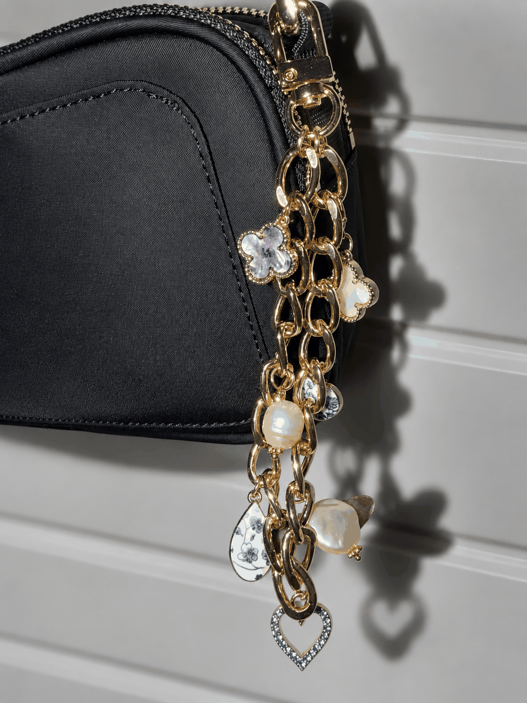 Gold chain charm with various pendants on a black handbag.