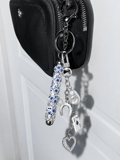 Handcrafted blue and white porcelain inspired beaded bag charm keychain with crystal horseshoe, Ace of Spades charm, pearl accent, and silver hardware displayed on a white background.