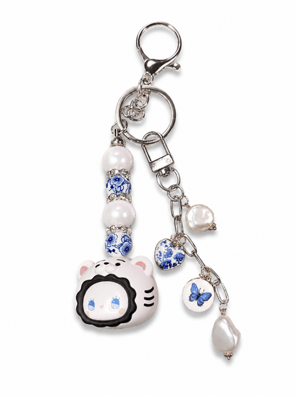 Authentic Emma Bean bag charm keychain with freshwater pearls, blue porcelain-inspired beads, butterfly charm, heart charm, and silver lobster clasp on a white background.