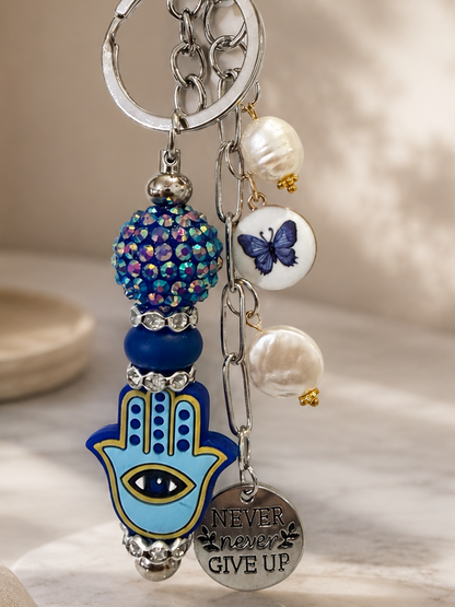 Blue Evil Eye Hamsa bag charm with freshwater pearls, butterfly charm, and "Never Give Up" pendant