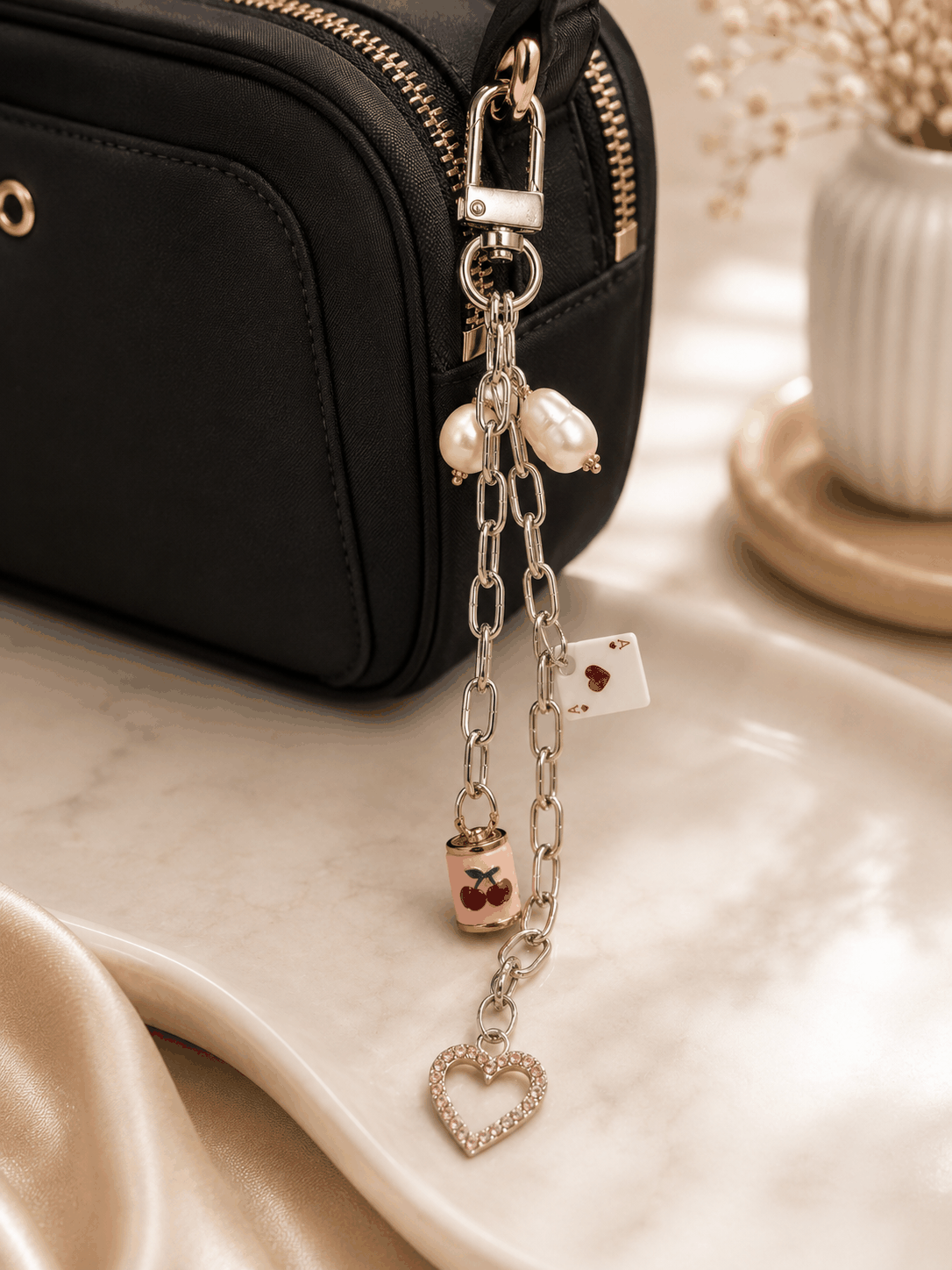 Cherry and Ace of Hearts bag charm with freshwater pearls, silver chain, pink crystal heart pendant, and silver lobster clasp displayed on a marble tray.