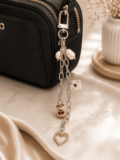 Cherry and Ace of Hearts bag charm with freshwater pearls, silver chain, pink crystal heart pendant, and silver lobster clasp displayed on a marble tray.