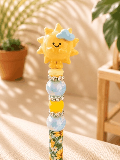 Authentic Meichai Sunshine Bean handmade beaded pen featuring a smiling sunshine topper, iridescent beads, yellow accent beads, rhinestone spacers, and a floral print ballpoint pen barrel.