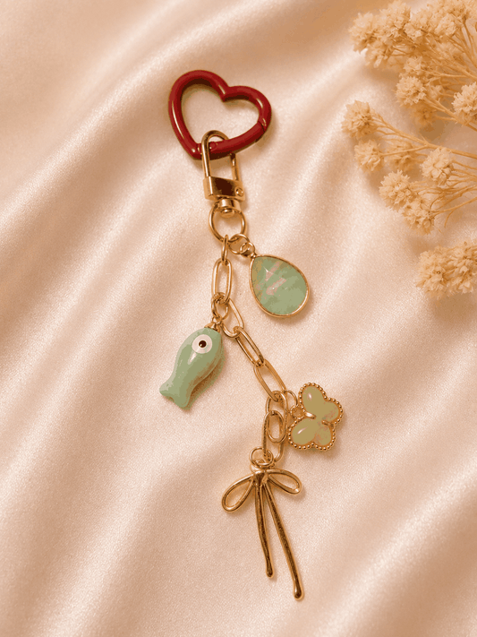 Handmade Mediterranean Heart Bag Charm with red heart clasp, seafoam gemstone, evil eye fish, gold bow, and clover accent